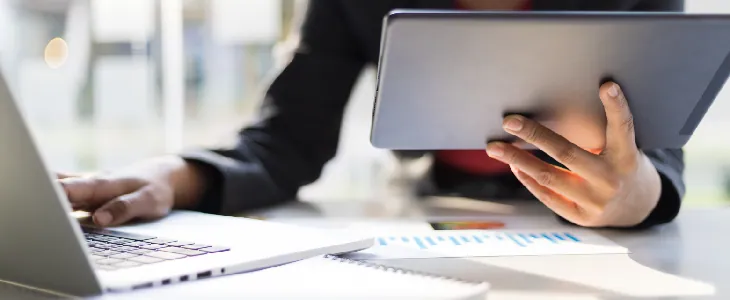 professional holding and looking at a tablet and typing on a laptop tax services